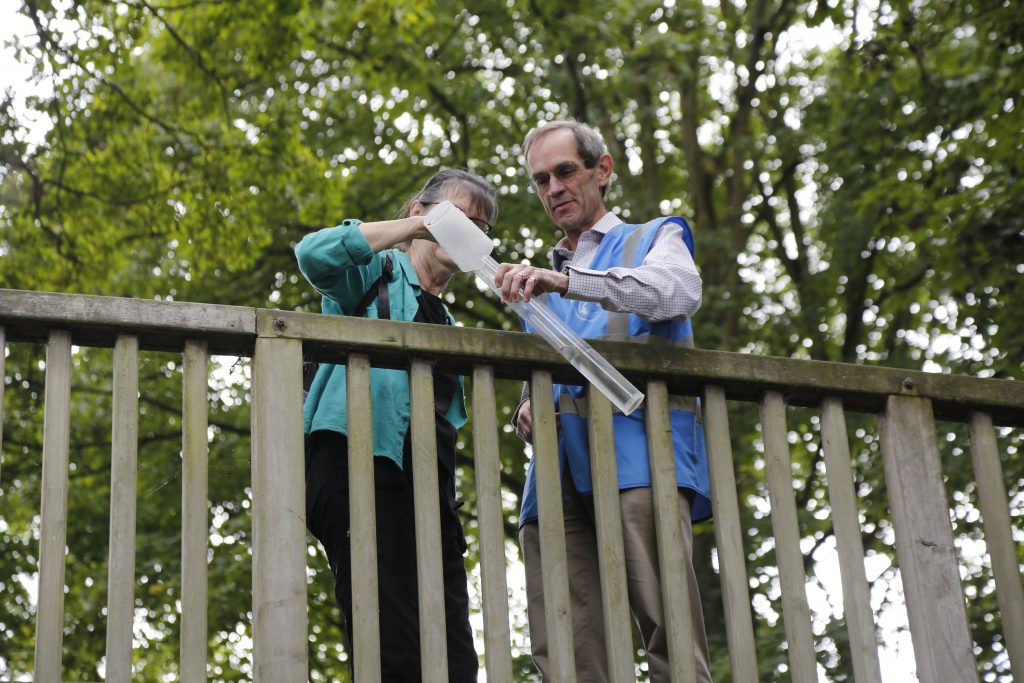 two volunteers stand on a bridge during water into a sampling tube